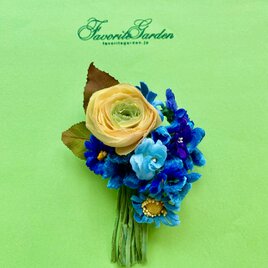 イエローのラナキュラスとブルーフラワーの花束コサージュの画像